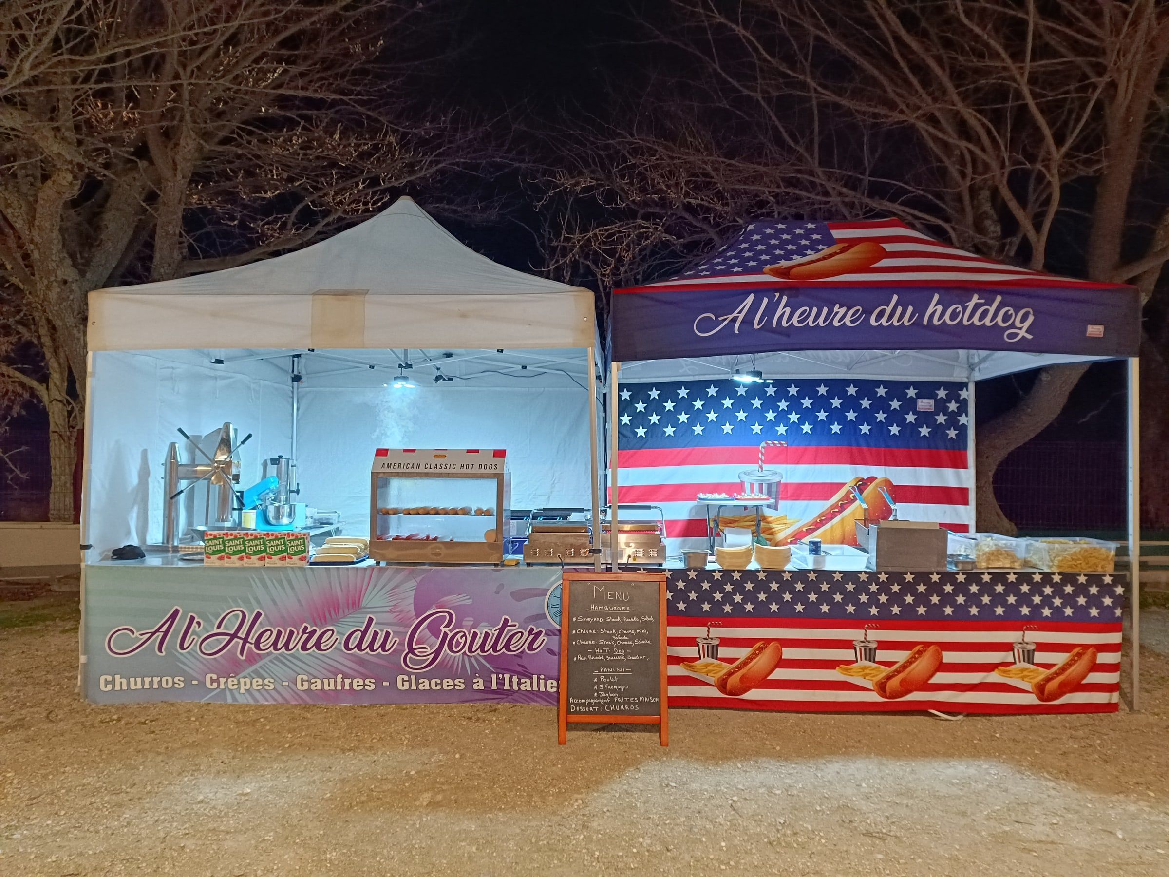La remorque A l’Heure du Goûter et le stand A l’heure du hotdog installés côte à côte, éclairés de nuit